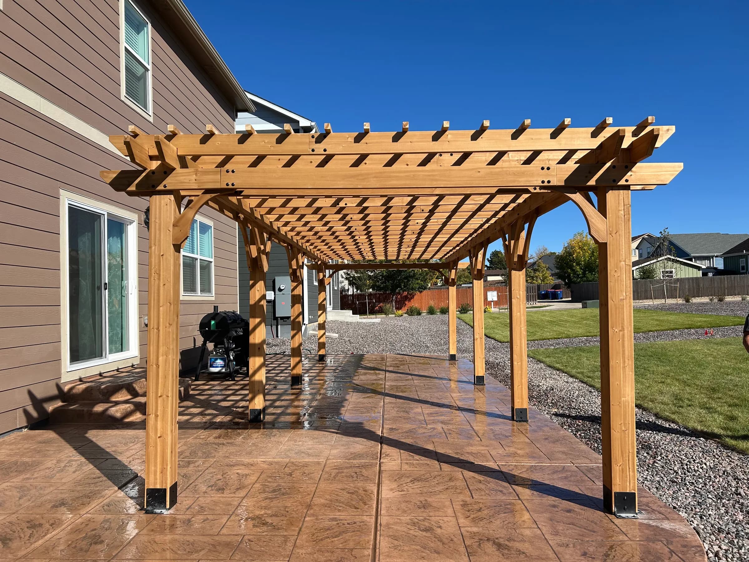 Cedar pergola over a stamped concrete patio beside a two-story house