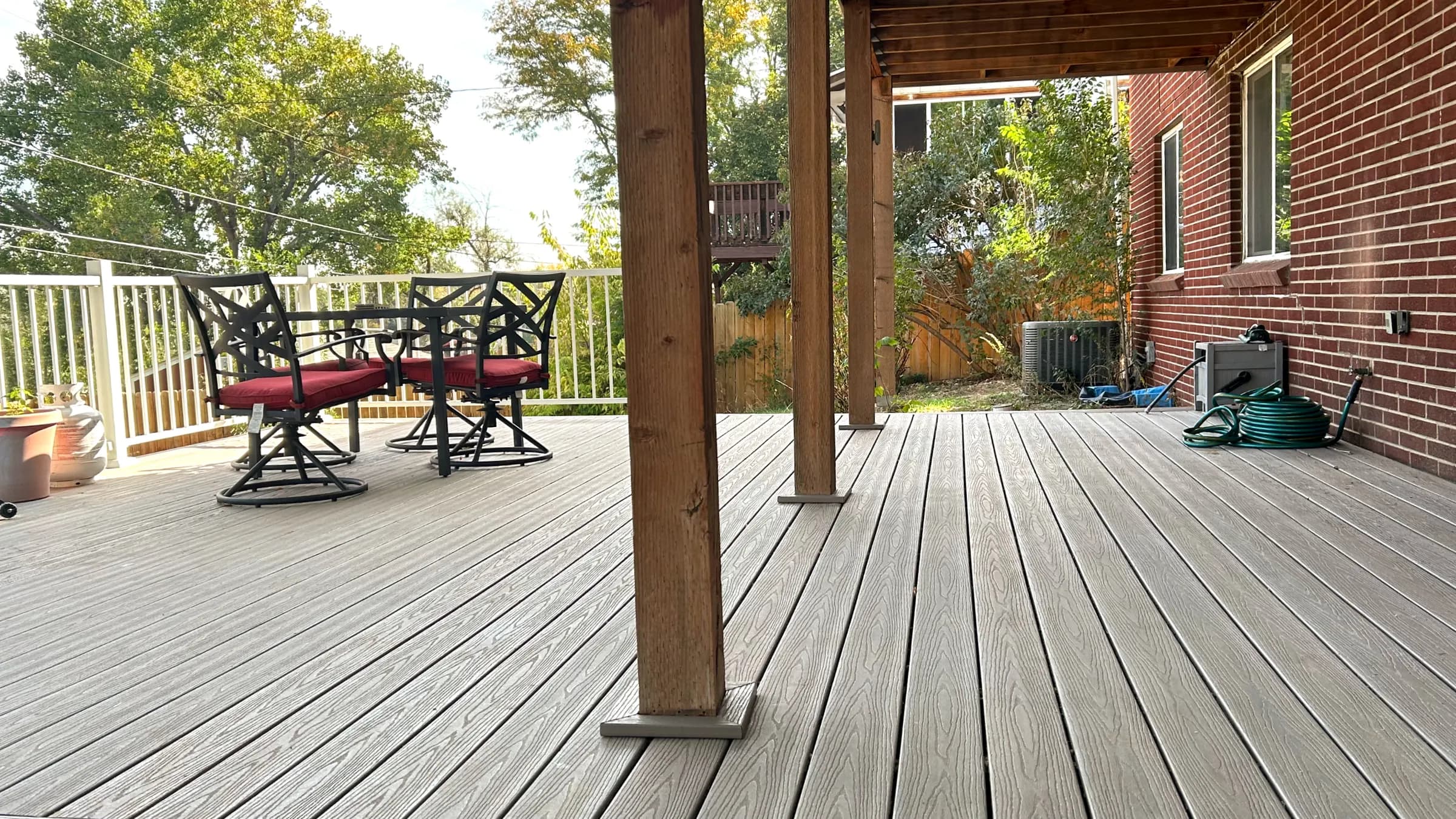 Covered composite deck with cedar posts beside a brick house