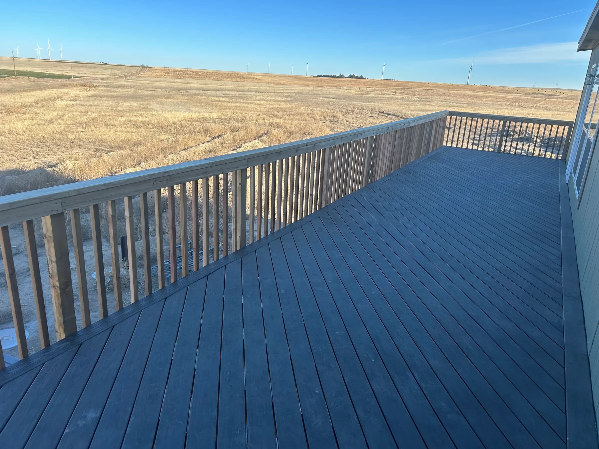 Gray deck with a wood railing looking out over open prairie